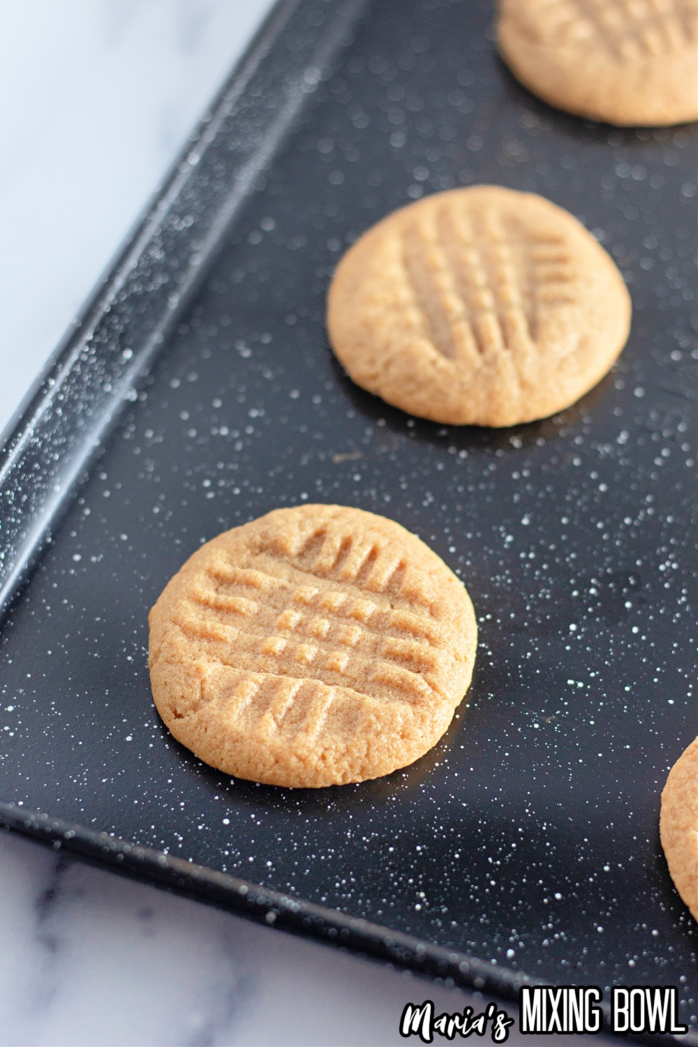 peanut butter cookies cooling on a dark baking dish