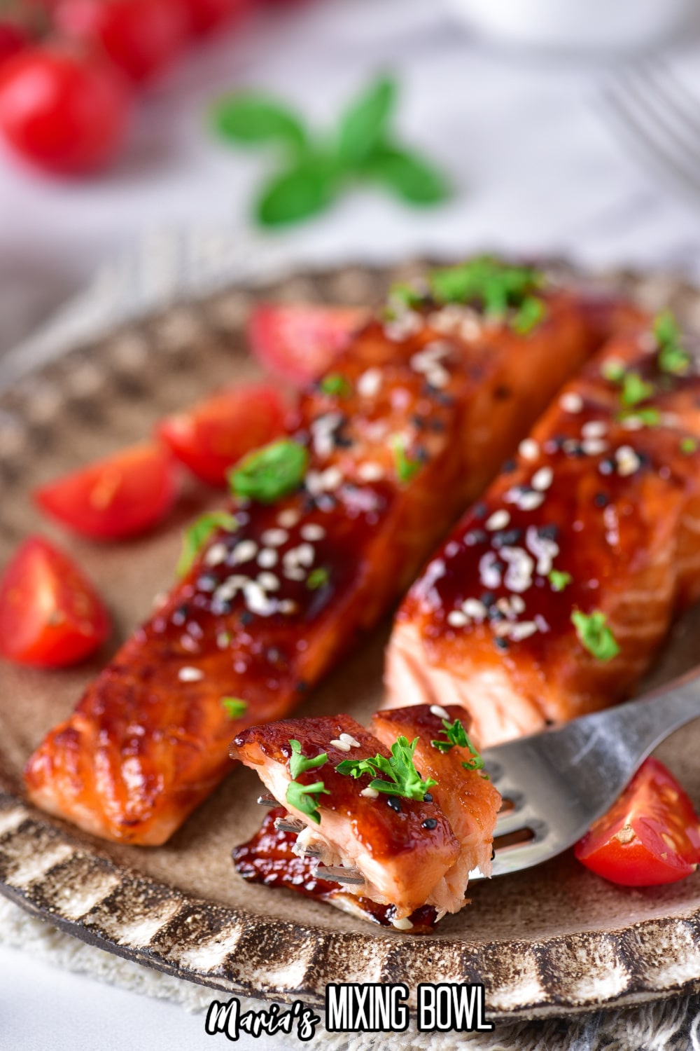 bite of teriyaki salmon garnished with sesame seeds, and fresh herbs on a fork