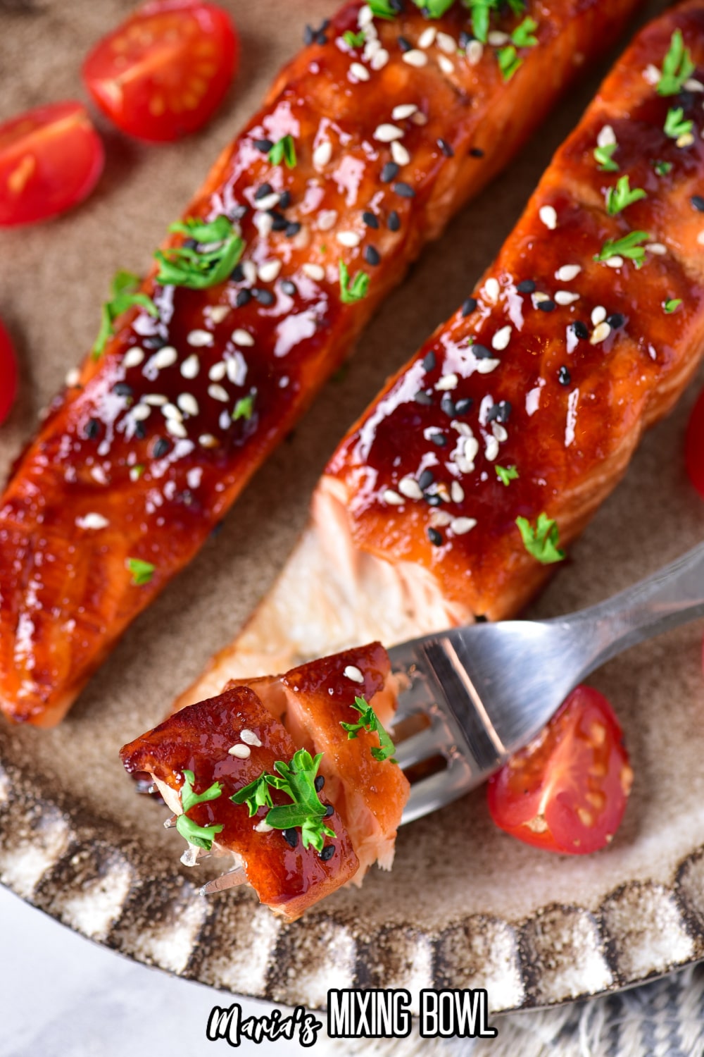 bite of teriyaki salmon garnished with sesame seeds, and fresh herbs on a fork