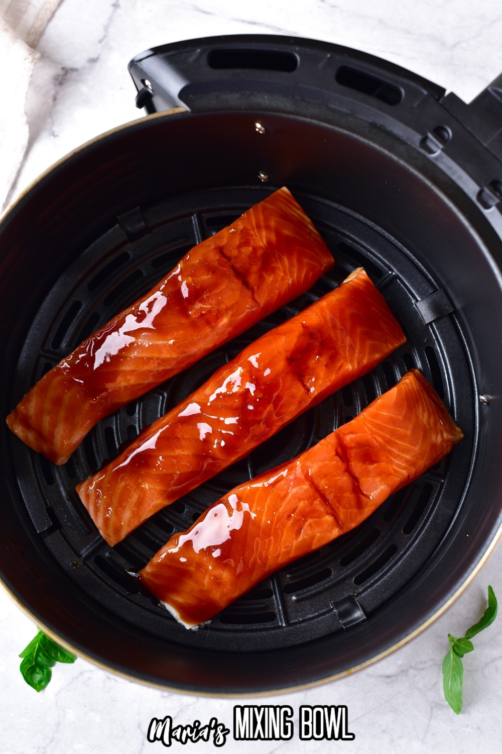 three raw salmon filets coated in teriyaki sauce in an air fryer basket.