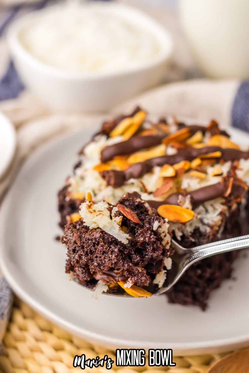 slice of almond joy poke cake on a white plate with a bite being removed with a spoon