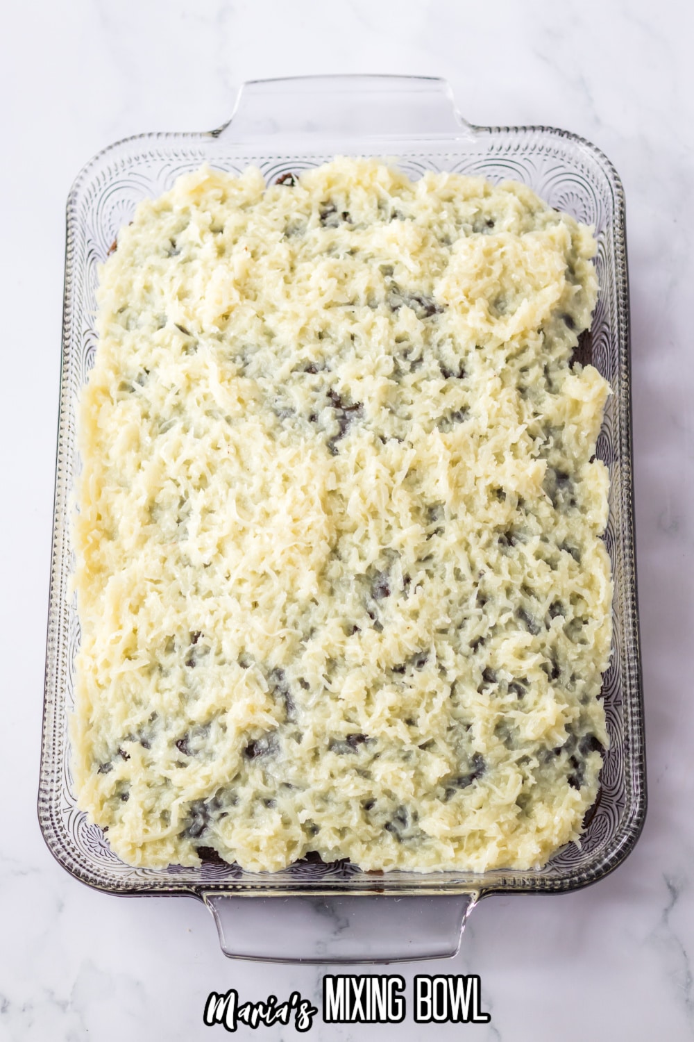 coconut being spread on top of a baked chocolate cake in a glass casserole dish