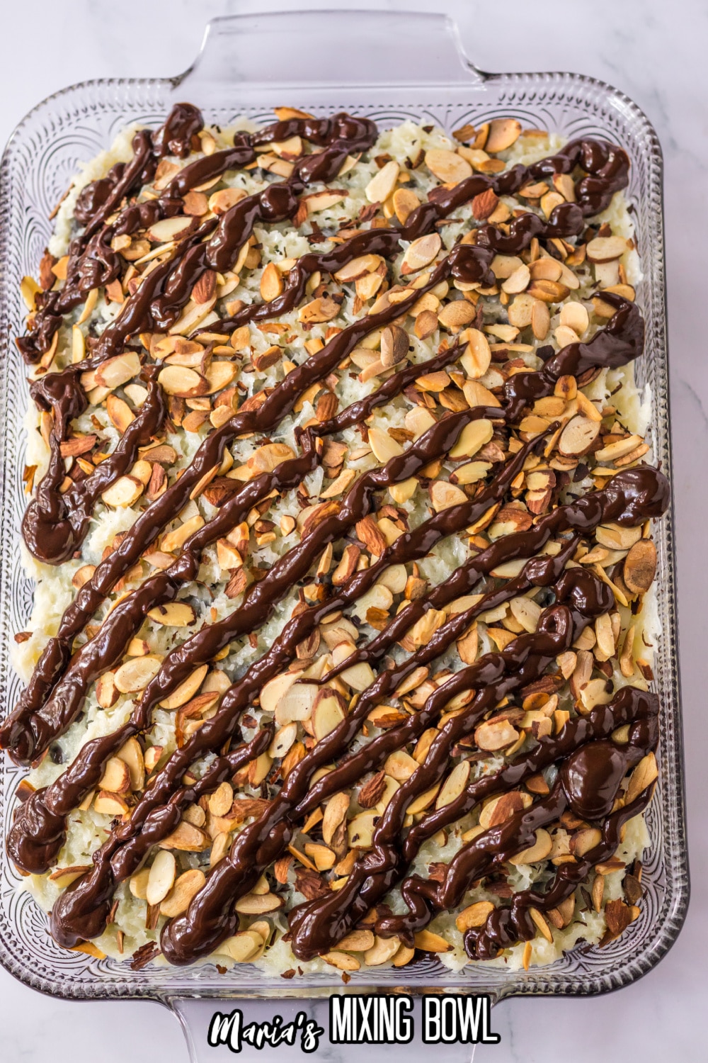 chocolate ganache being piped on top of the cake in a glass baking dish