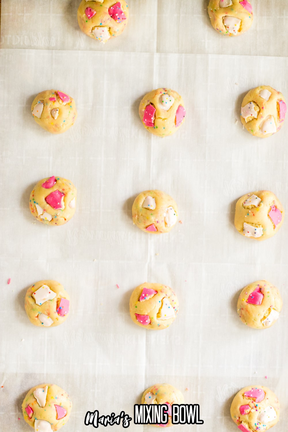 raw cookie dough balls with pieces of Circus Animal Cracker cookies pressed into them on a parchment lined baking sheet.
