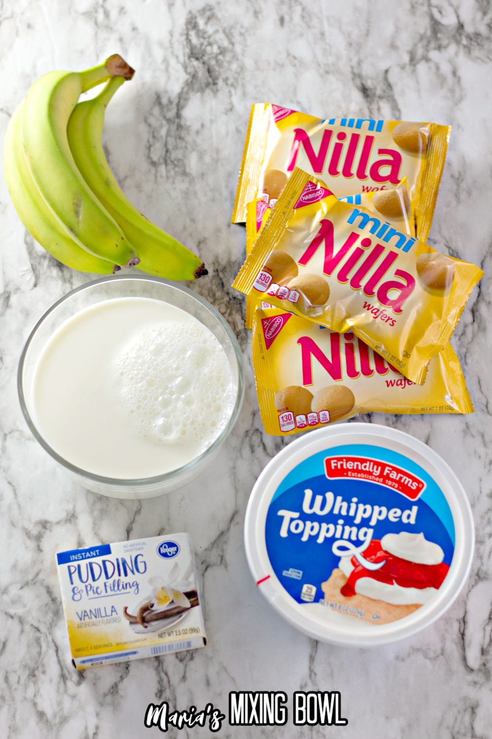 mini nilla wafer packages, whipped toppings, bananas, vanilla pudding mix and bowl of milk on a marble background