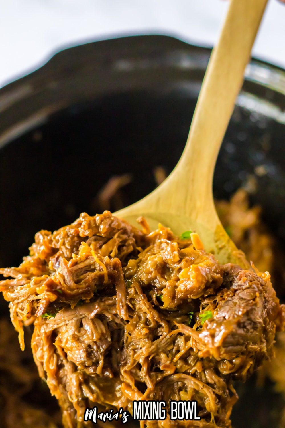 large wooden spoon full of shredded beef held in the air.