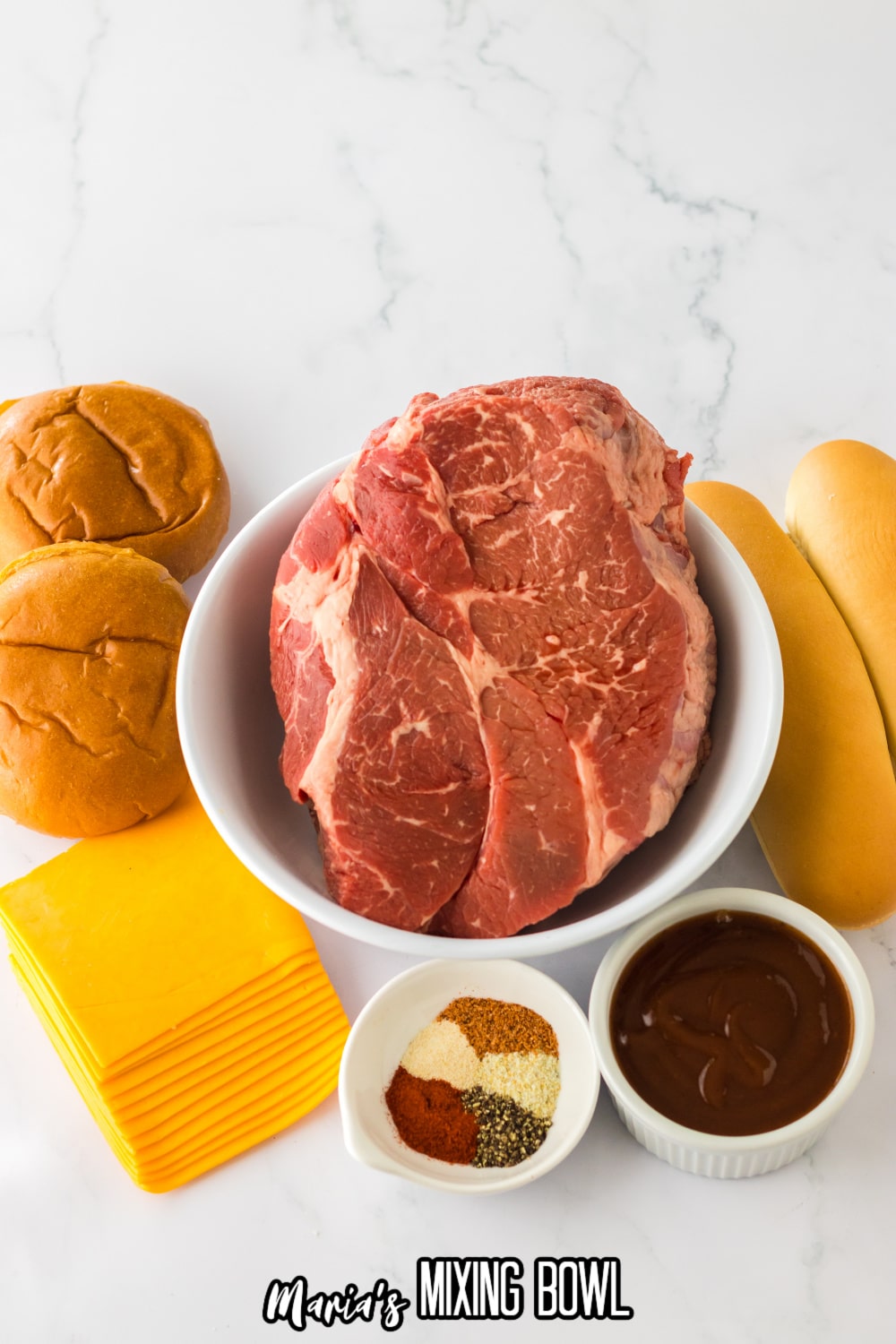 large bowl of raw chuck roast, small bowls of seasoning and bbq sauce, with sliced cheese, and buns around it.