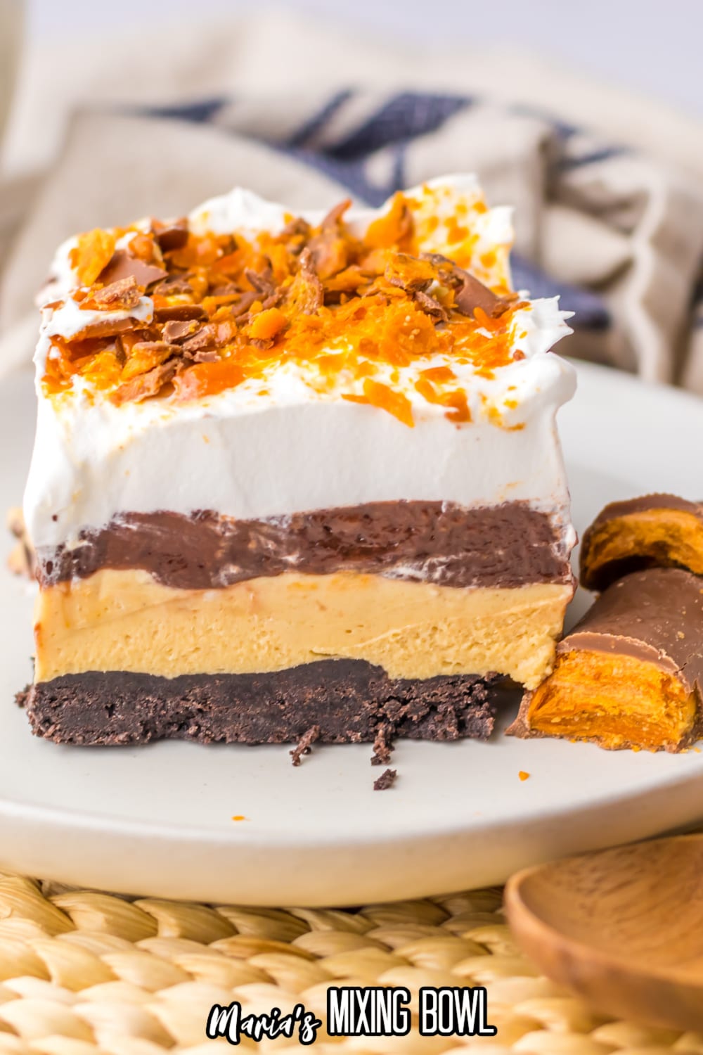 slice of butterfinger lush on a white plate with two butterfinger bars beside it.