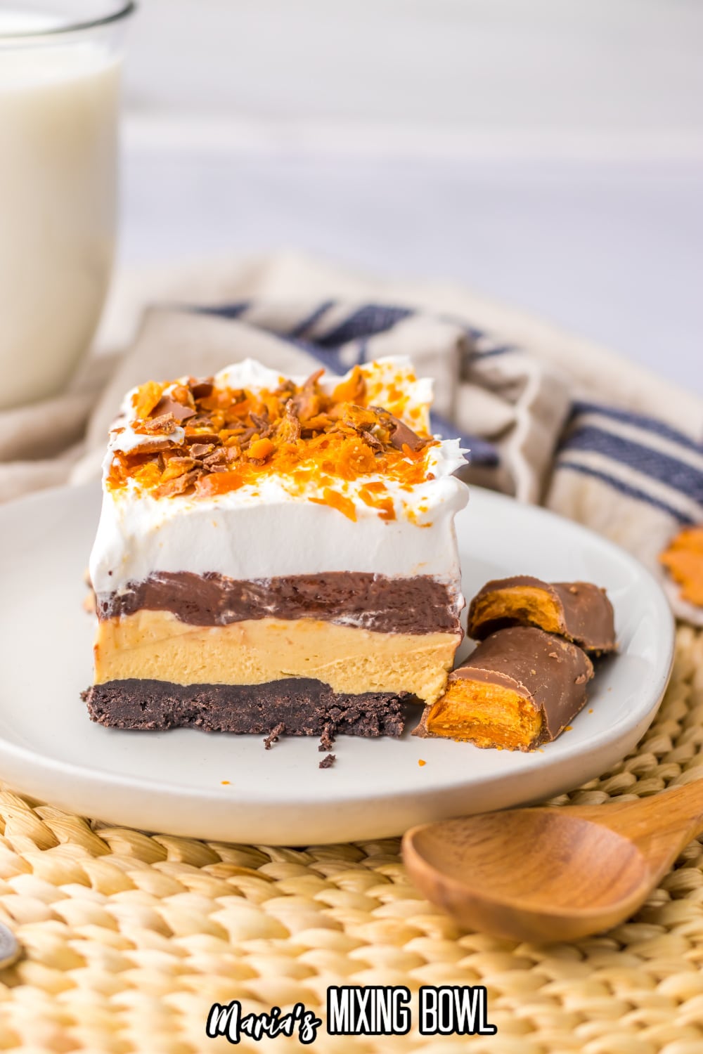 slice of butterfinger lush on a white plate with two butterfinger bars beside it.