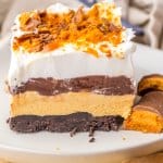 slice of butterfinger lush on a white plate with two butterfinger bars beside it.