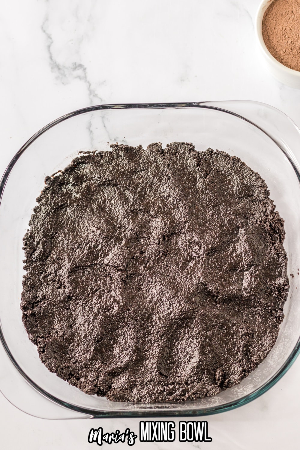 oreo crust being pressed into the bottom of the glass baking dish