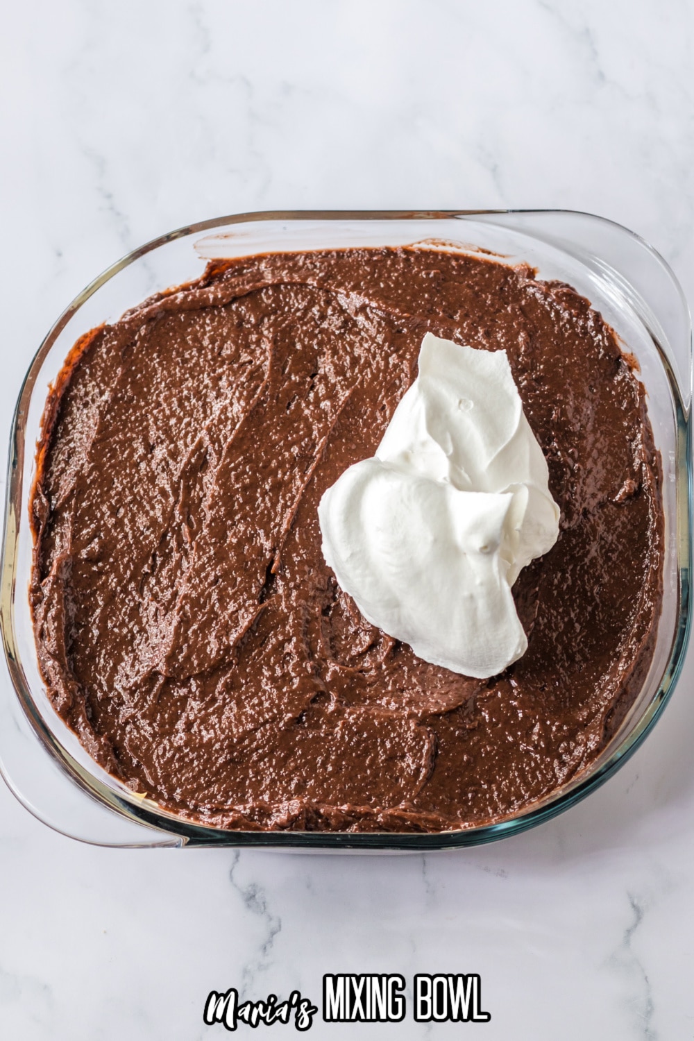 chocolate pudding and whipped topping being spread on a top of a casserole dish