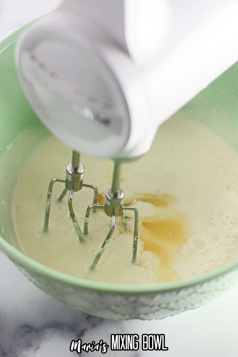 cheesecake filling being mixed with a hand mixer in a green mixing bowl
