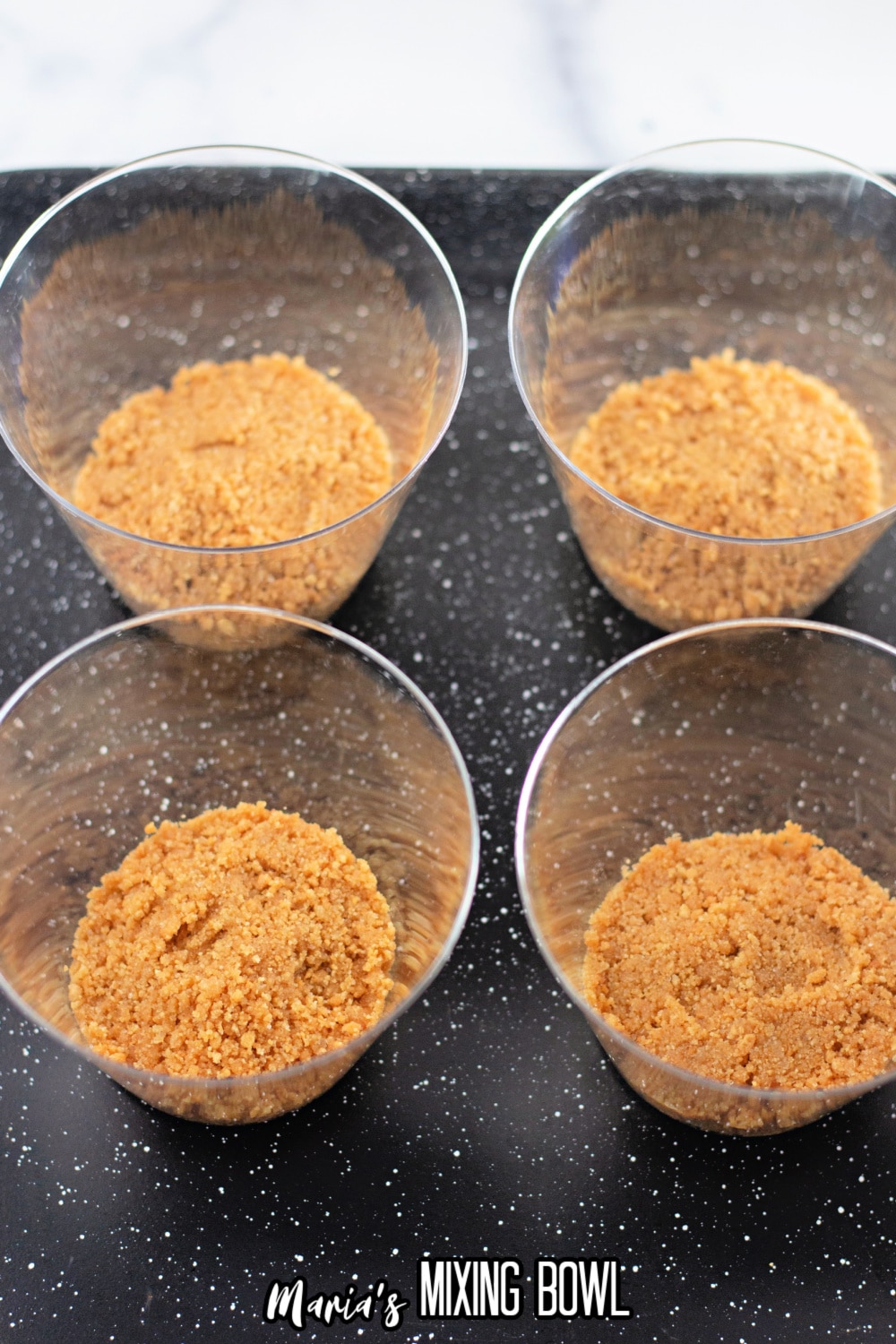 graham cracker crumbs being added to small plastic cups