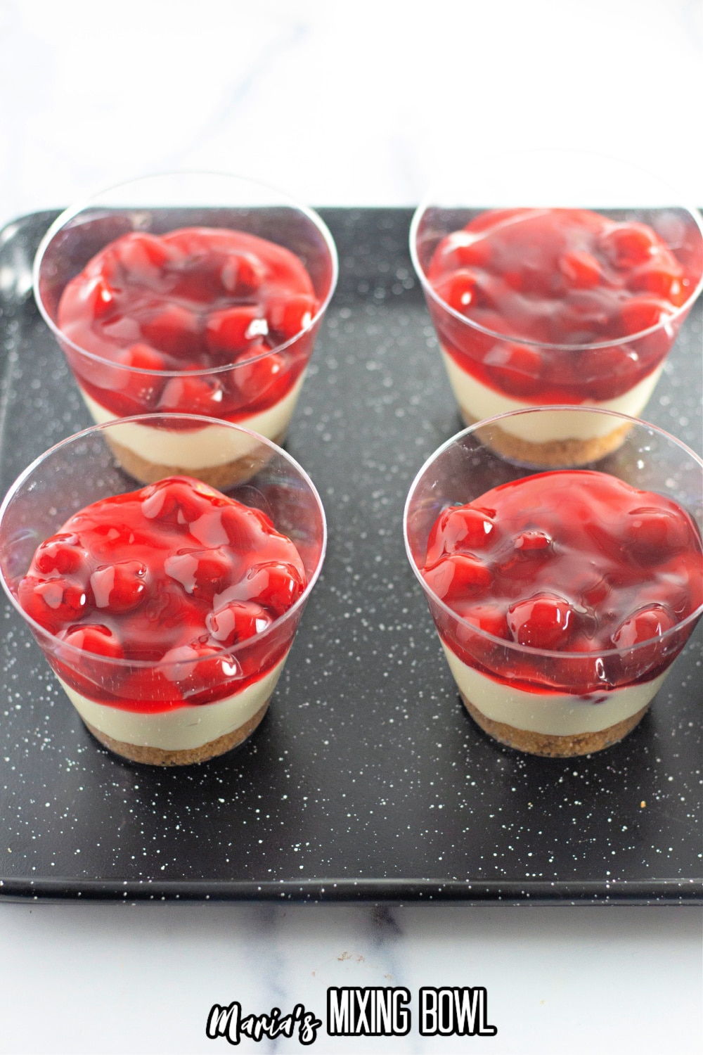 cups being layered with cherries, cheesecakes and graham crackers