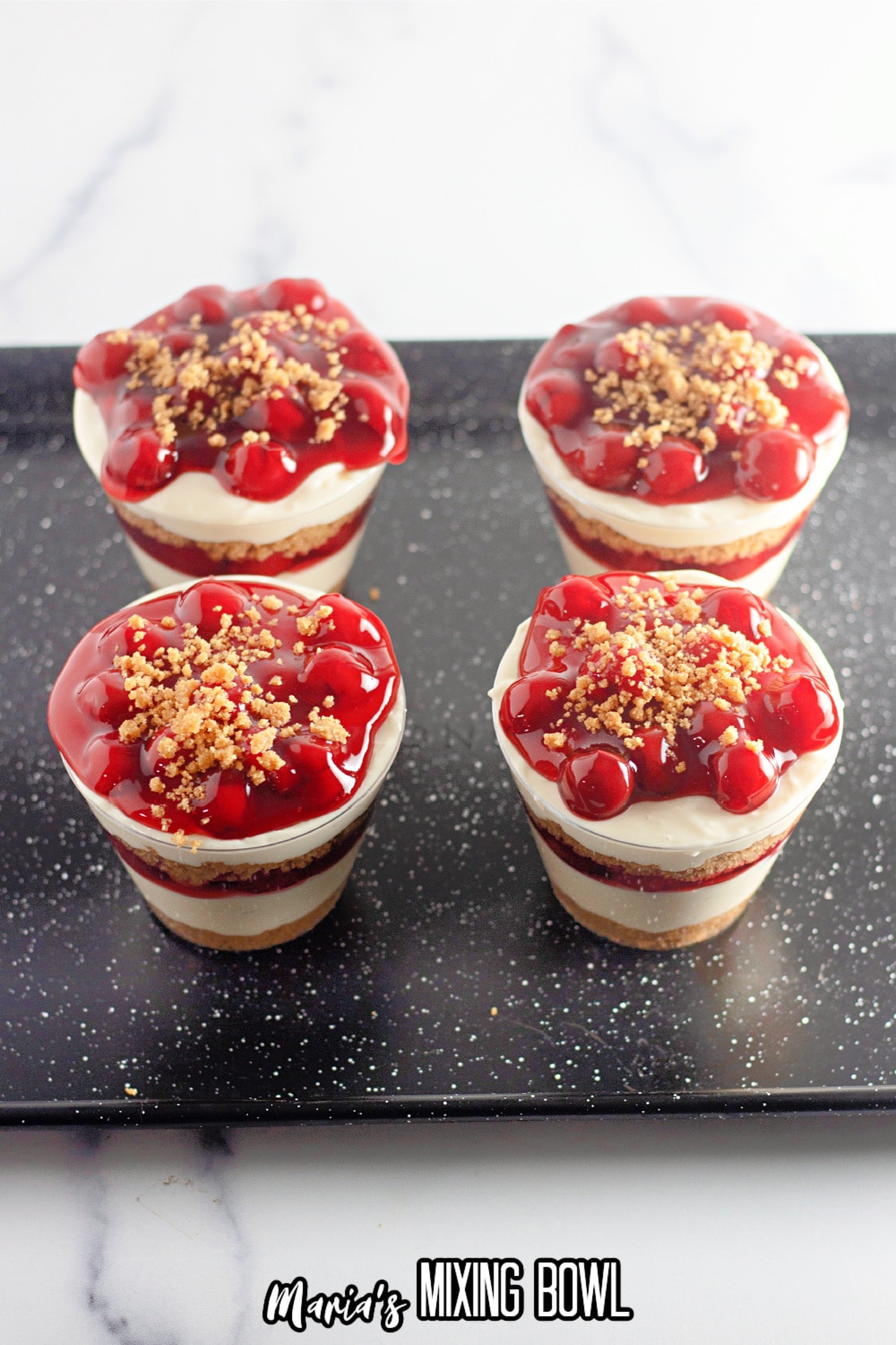 four finished cherry cheesecake cups on a dark baking sheet