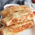 slices of stromboli on a white rectangular platter with a jar of pasta sauce