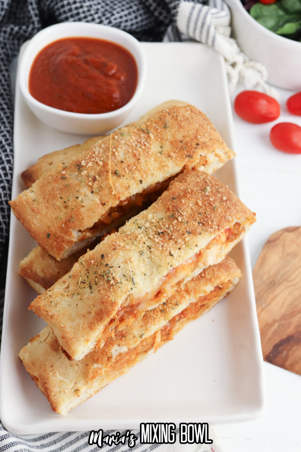 slices of stromboli on a white rectangular platter with a jar of pasta sauce