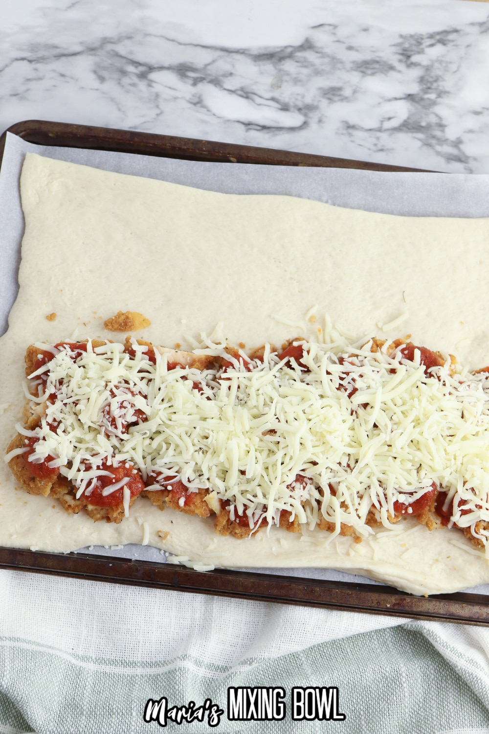pizza dough roll out, and filled with chopped chicken tenders, pizza sauce, and shredded cheese on a baking sheet