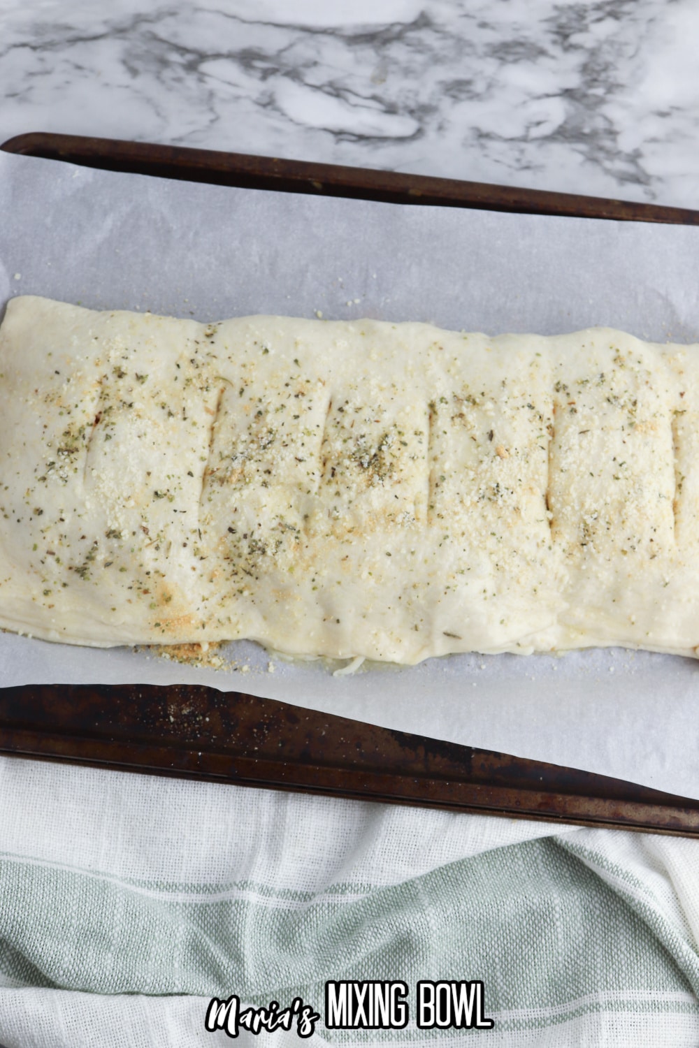 stromboli being seasoned and sliced on a parchment lined baking sheet
