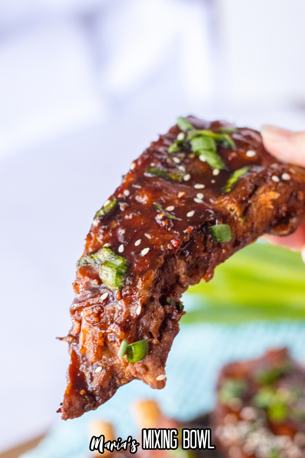 chinese spare rib held in the air topped with sesame seeds and green onions