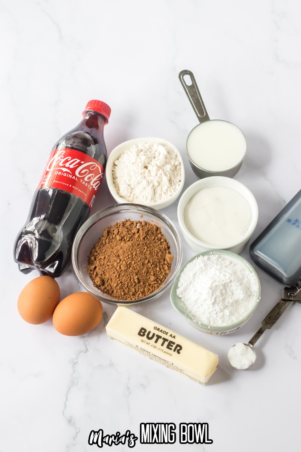 bottle of coke, bowls of flour, sugar, cocoa powder, milk, powdered sugar, eggs, butter, vanilla extract, baking powder