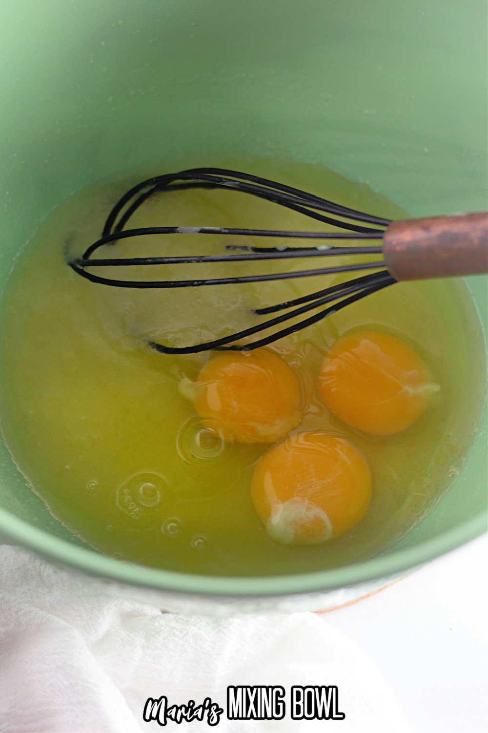 eggs and sugar being whisked in a green mixing bowl