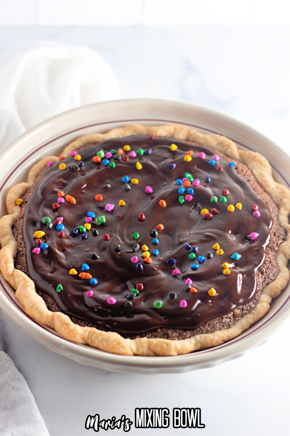 uncut brownie pie in a white pie plate with rainbow sprinkles on top