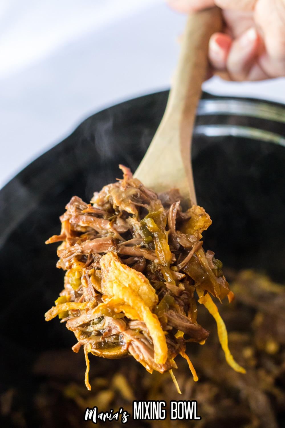 spoonful of shredded beef and fried onions on a wooden spoon held about the slow cooker