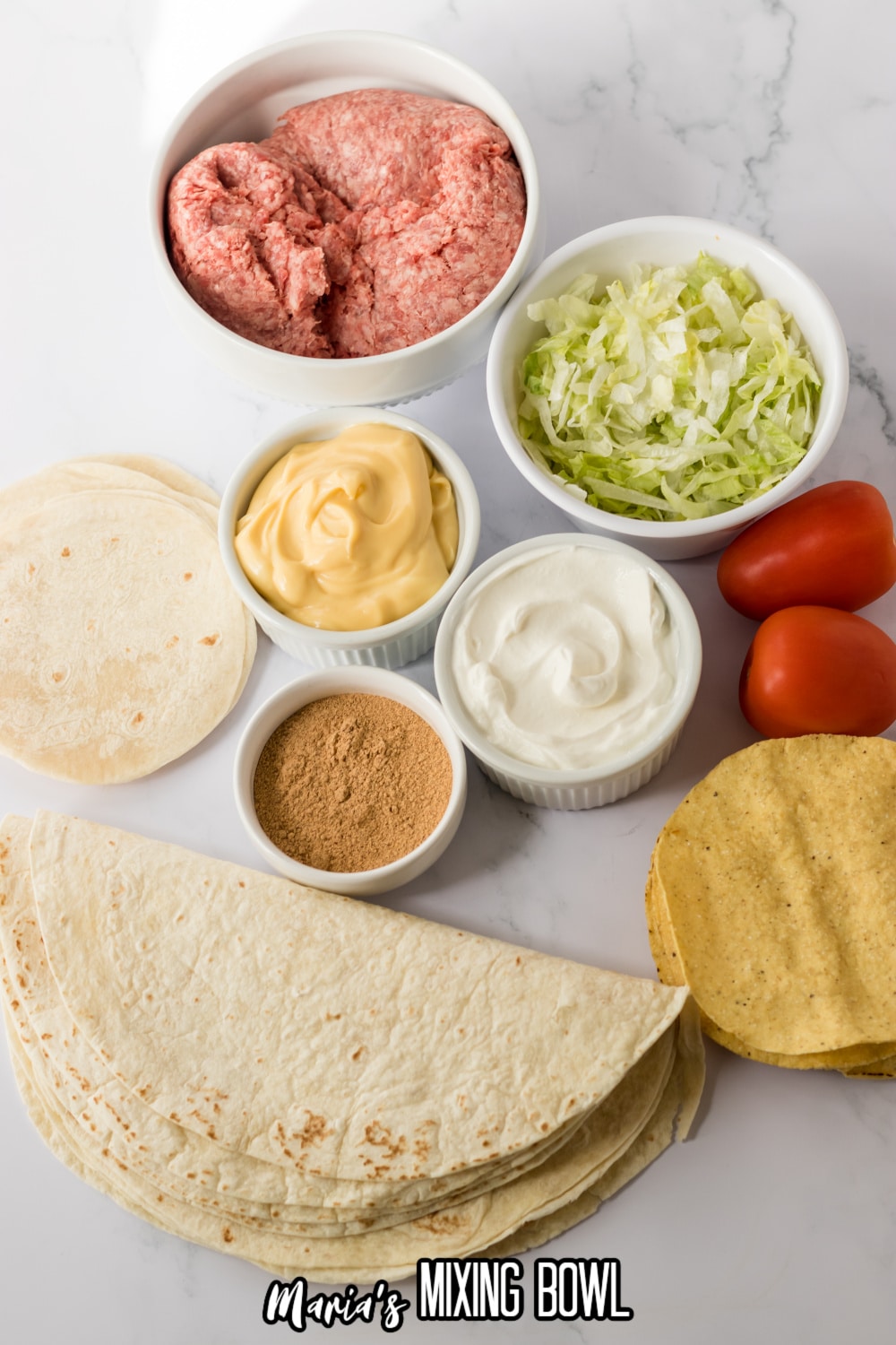 bowls of raw ground beef, shredded lettuce, nacho cheese, sour cream, taco seasoning, and tortillas, and tomatoes around them.