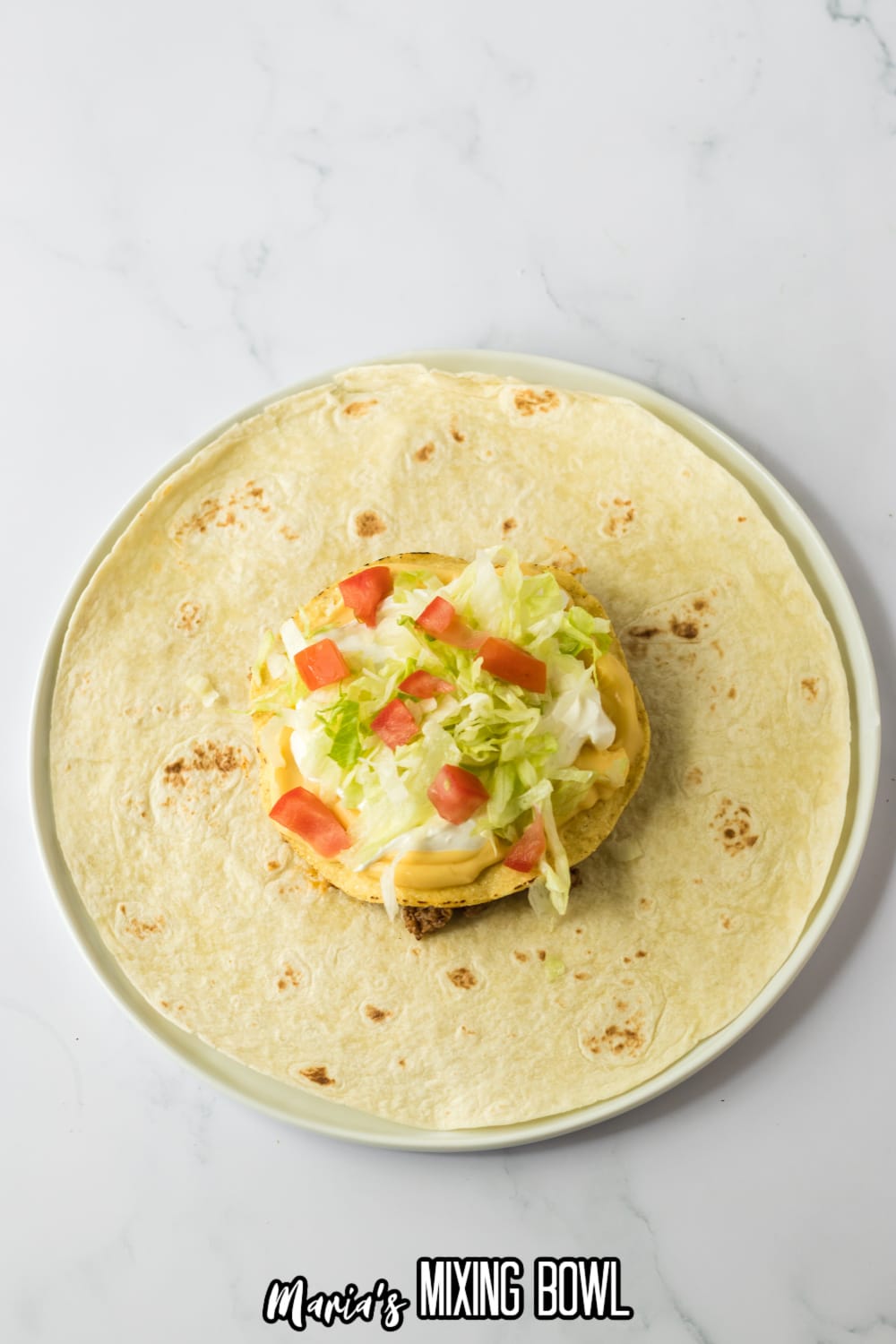 taco fillings being layered on top of a large tortilla.