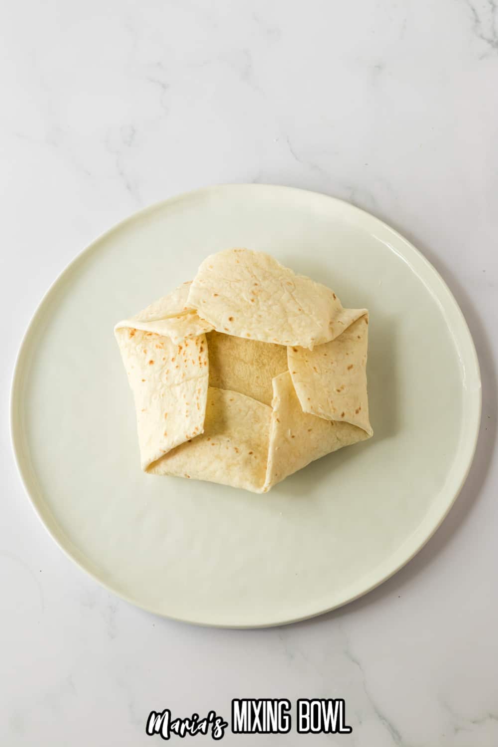 tortilla being folded around a crunchwrap on a plate.