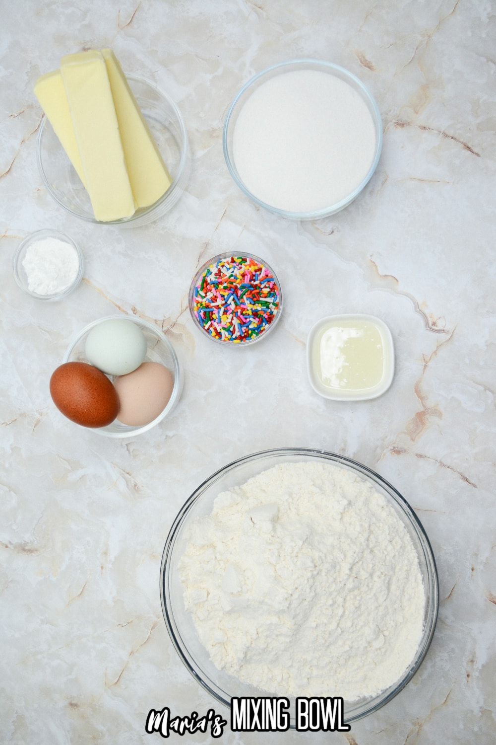 bowls of butter, sugar, cake mix, sprinkles, oil, and eggs on a marble counter top