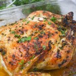 whole roasted chicken topped with fresh parsley in a glass baking dish
