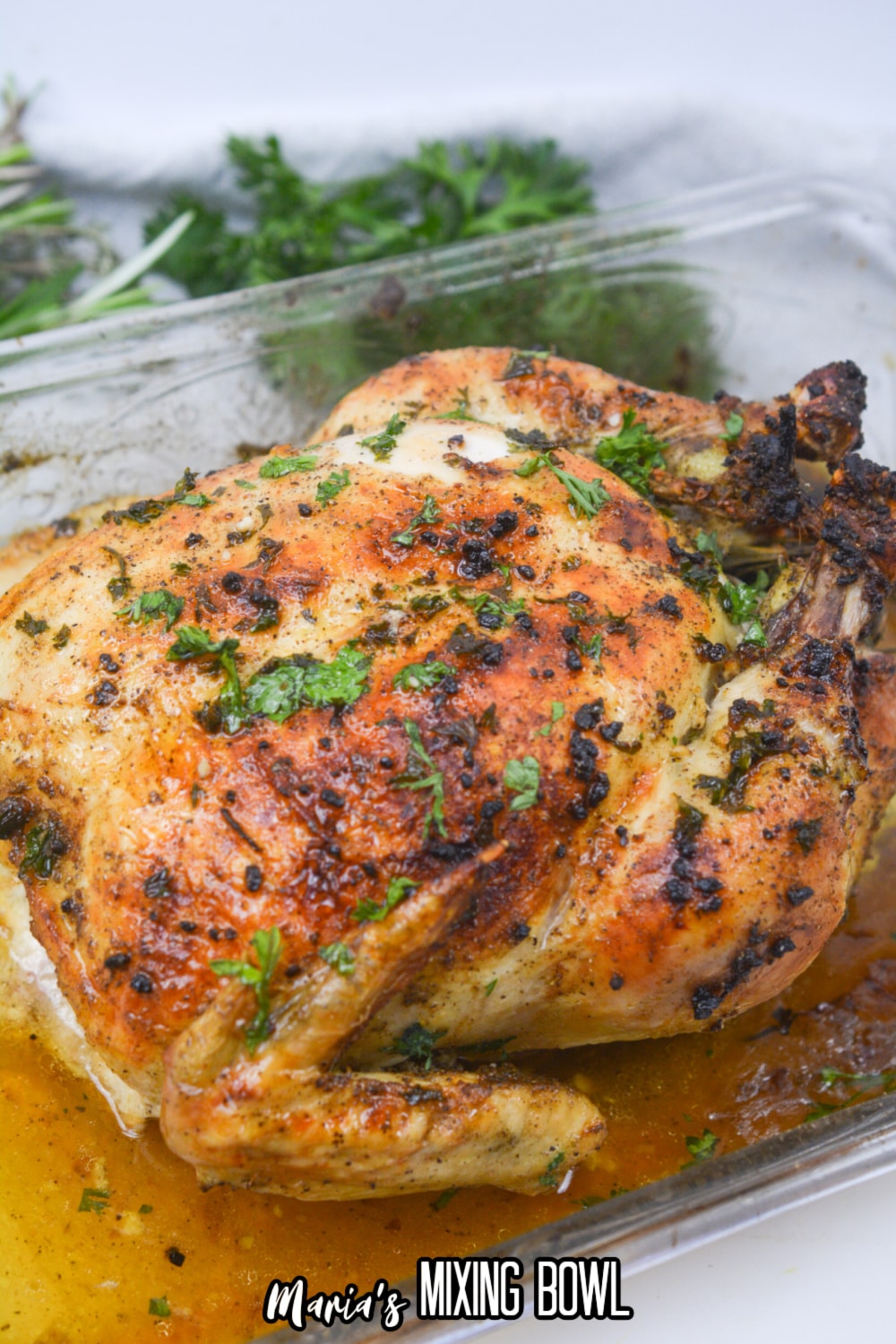 whole roasted chicken topped with fresh parsley in a glass baking dish