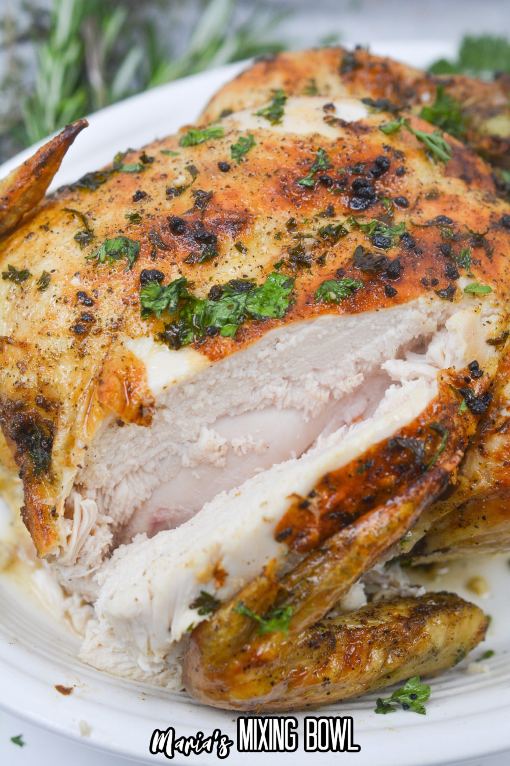 whole chicken on a white platter with a slice craved out of it.