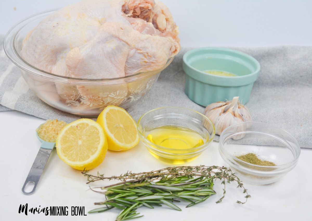 whole chicken, melted butter, oil, lemon sliced in half, minced garlic, and seasonings on a white background