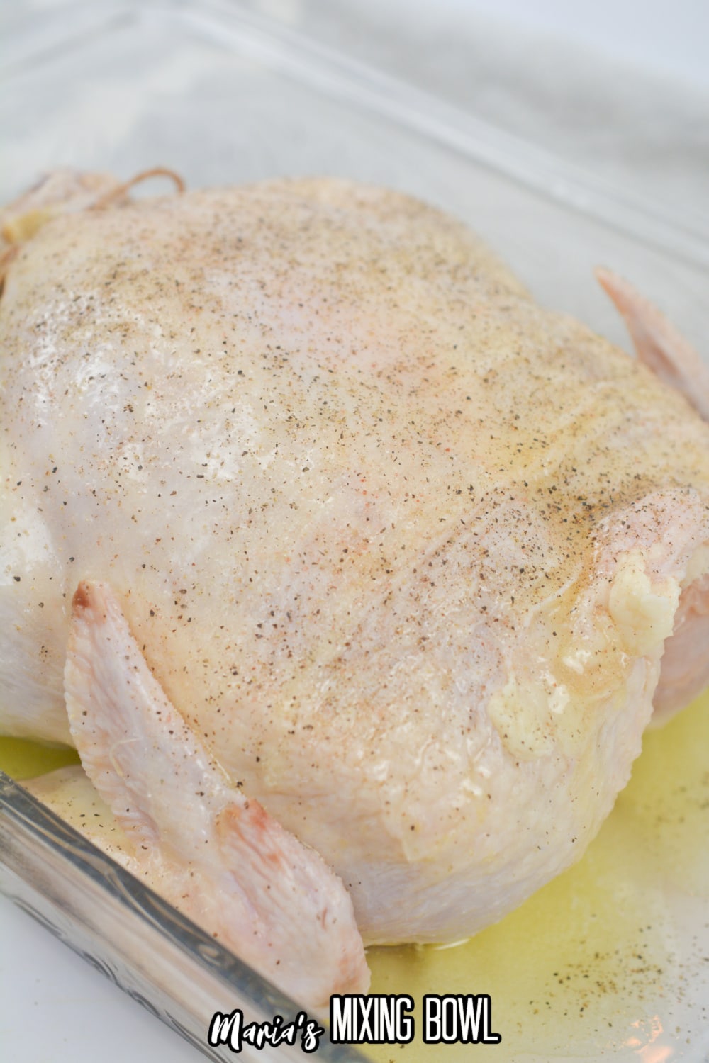 whole chicken rubbed with butter and oil and seasoned with pepper in a glass baking dish