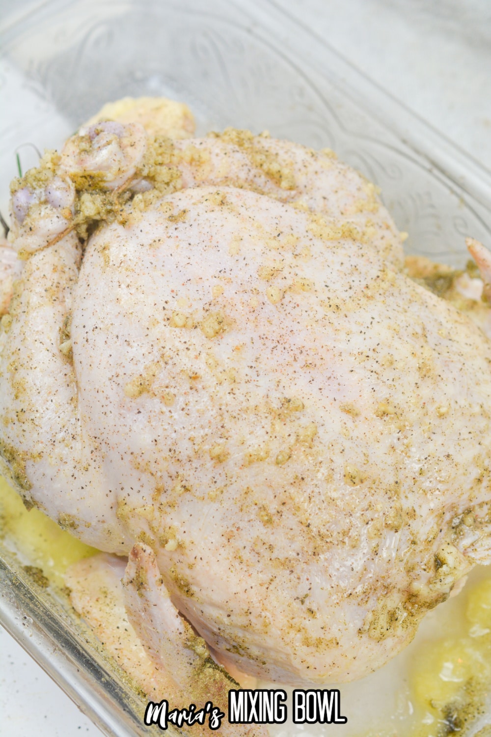 seasonings rubbed on a raw whole chicken in a glass baking dish