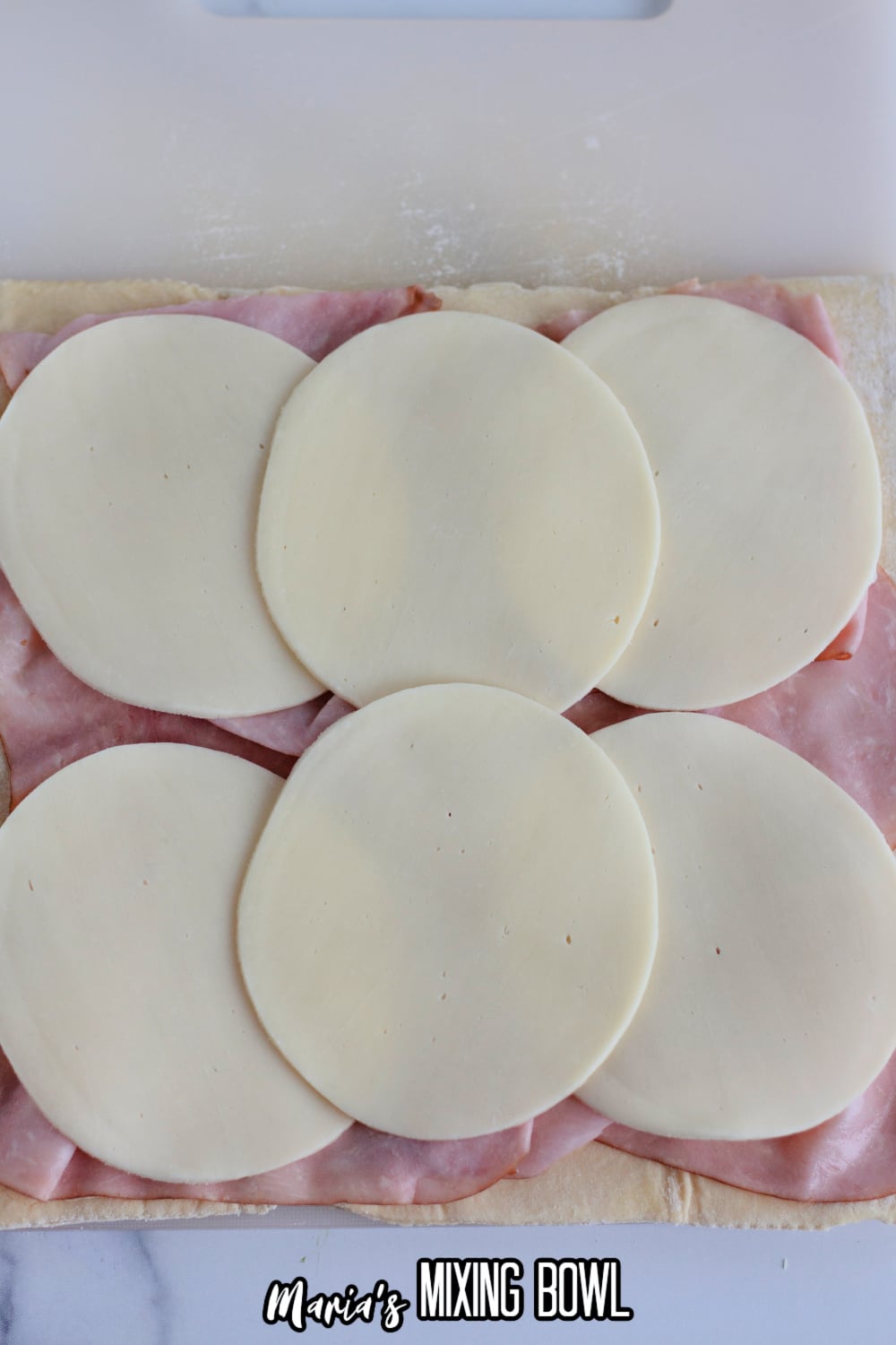 ham and provolone cheese being layered on a puff pastry
