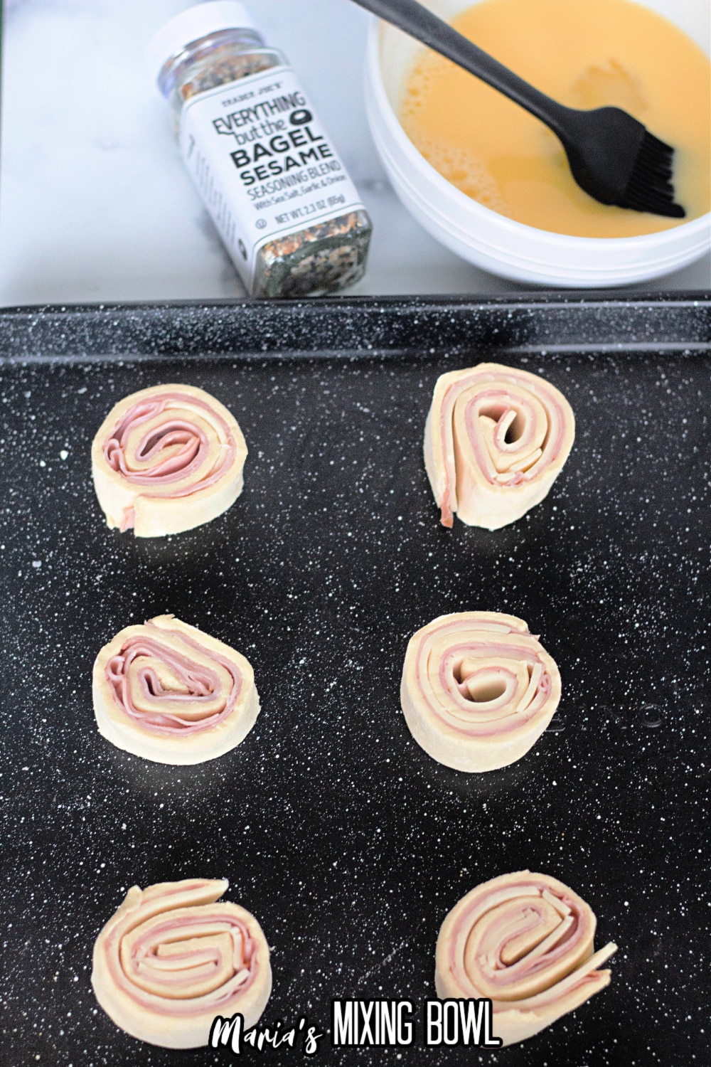 unbaked pinwheels being brushed with an eggwash and sprinkled with everything bagel seasoning
