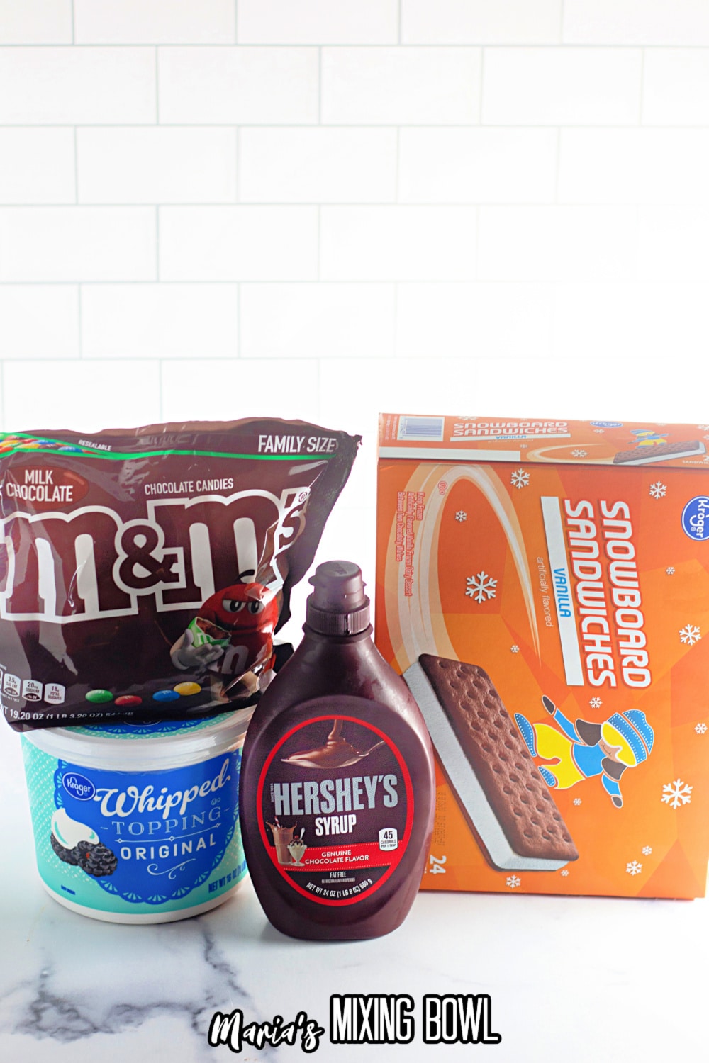 a bag of m&m's, container of whipped topping, bottle of hershey syrup and box of ice cream sandwiches on a marble background