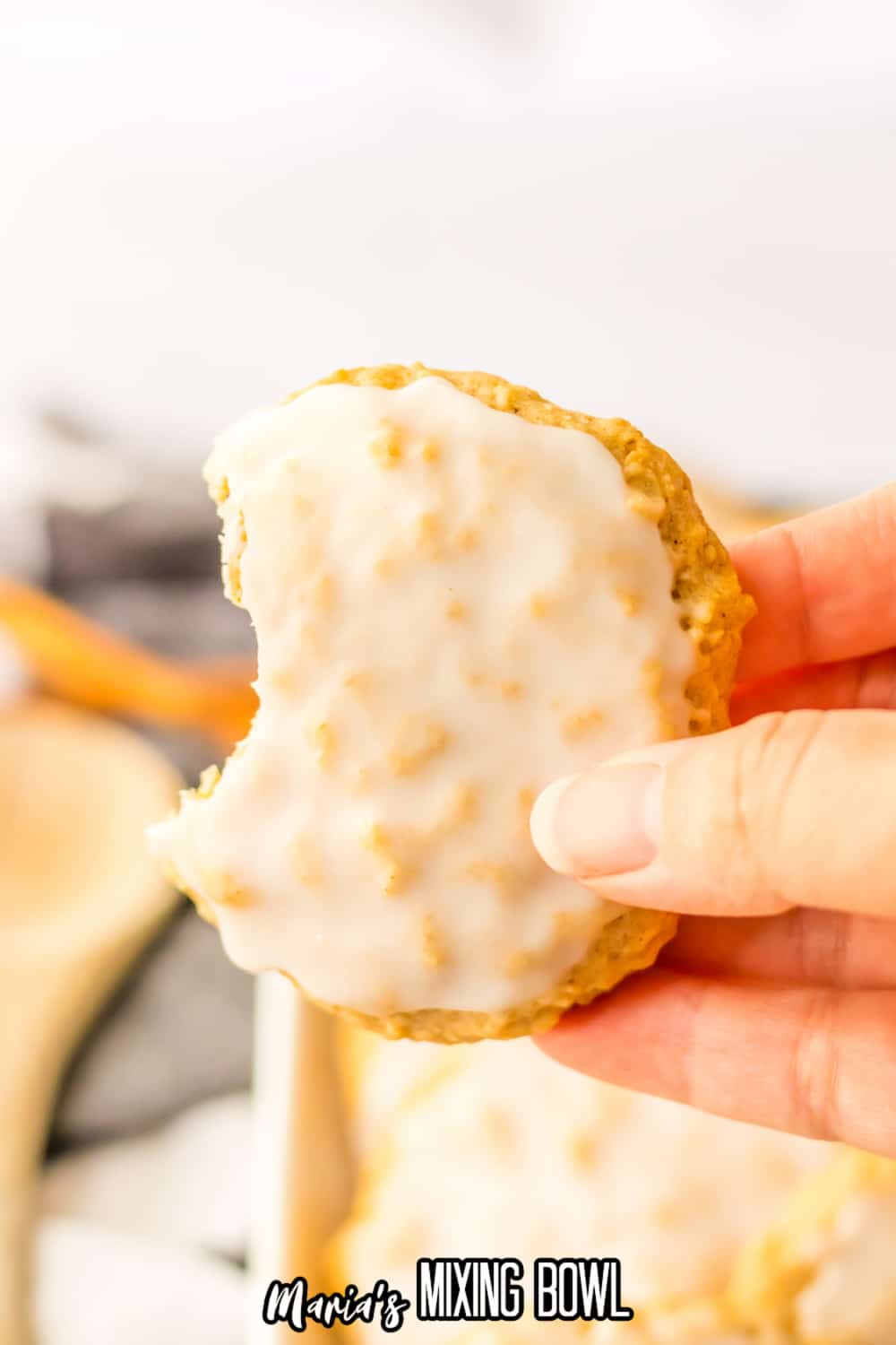 single iced oatmeal cookie held in the air in a woman's hand with a bite missing