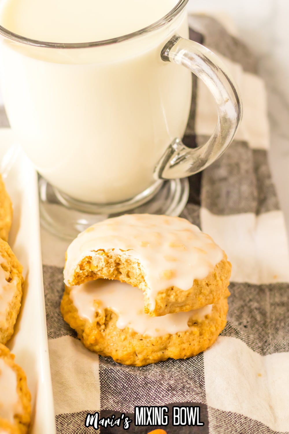 two iced oatmeal cookies stacked on a black and white checkered napkin the top cookie has a bite missing