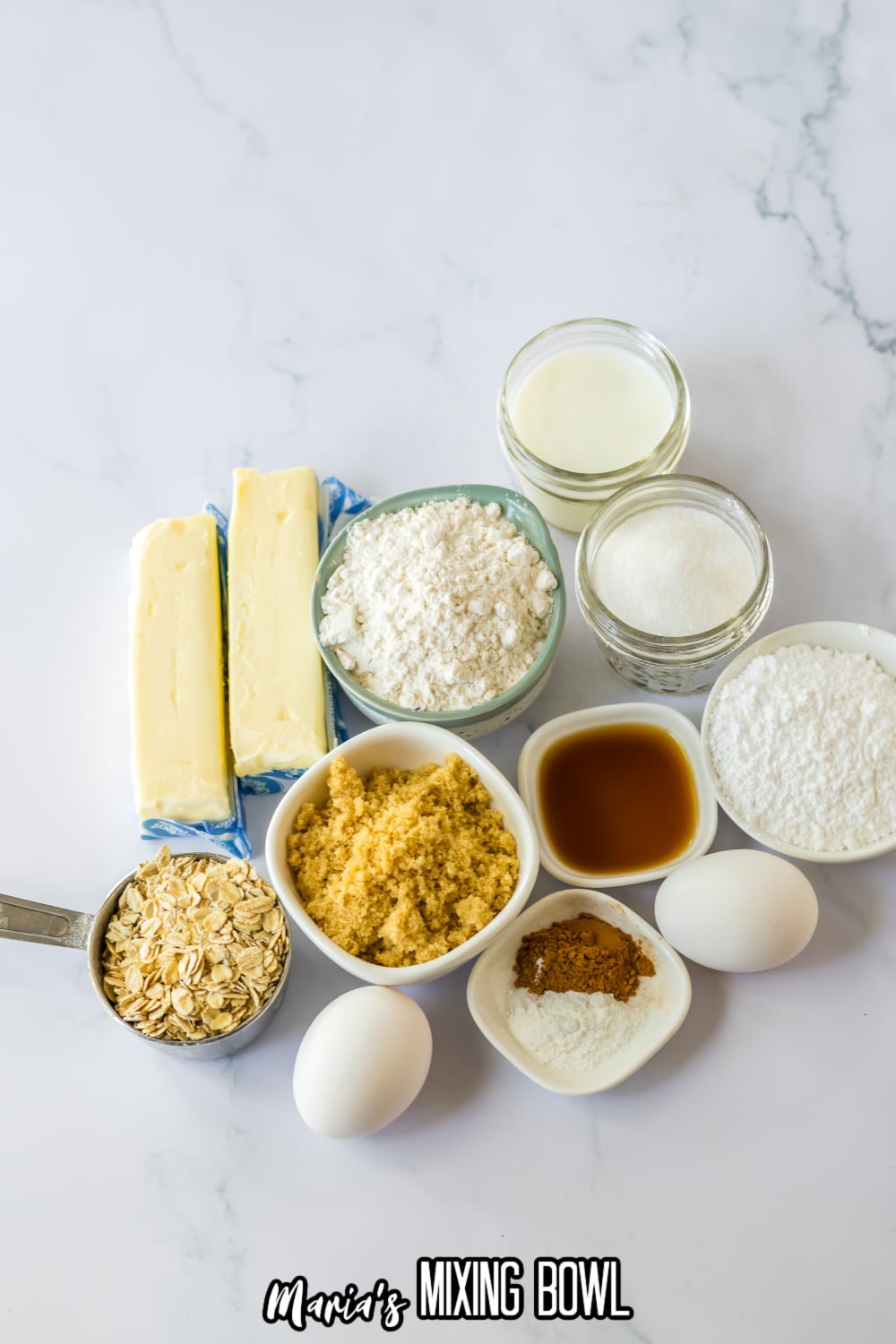 bowls of flour, butter, brown sugar, oats, eggs, cinnamon, salt, baking powder, powdered sugar, granulated sugar, and milk on a white background