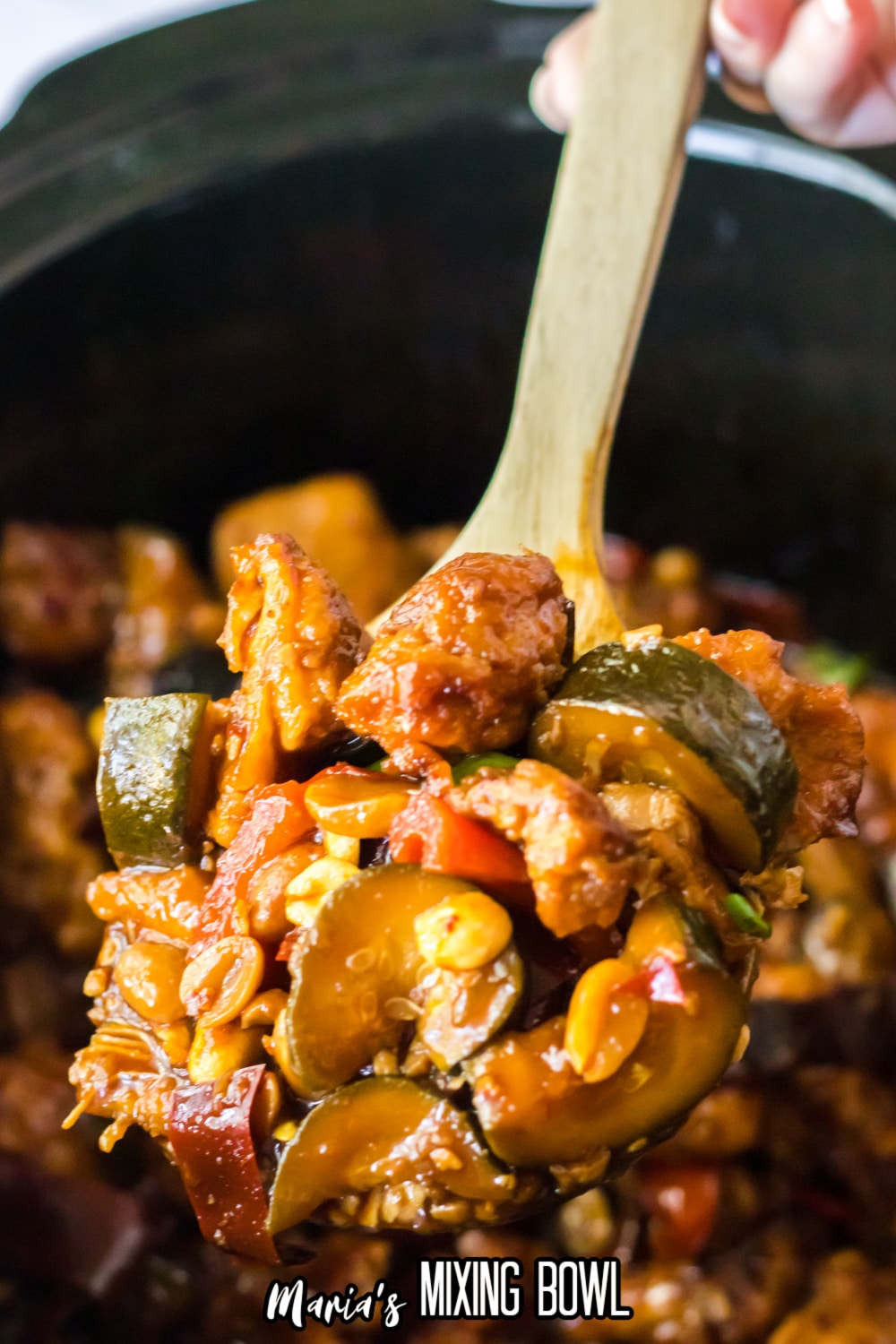 large wooden spoonful of kung pao chicken held above a slow cooker