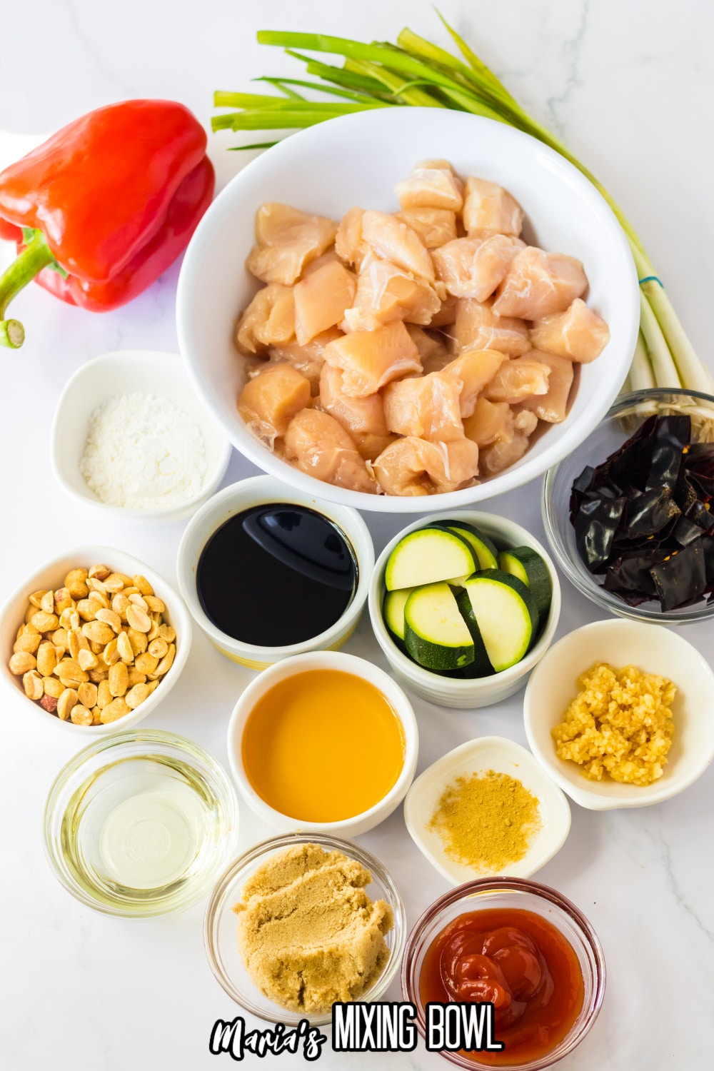 bowls of raw chicken, sliced zucchini, peanuts, brown sugar, cornstarch, oil, red chilies, garlic, ginger, ketchup, bell pepper and green onions.