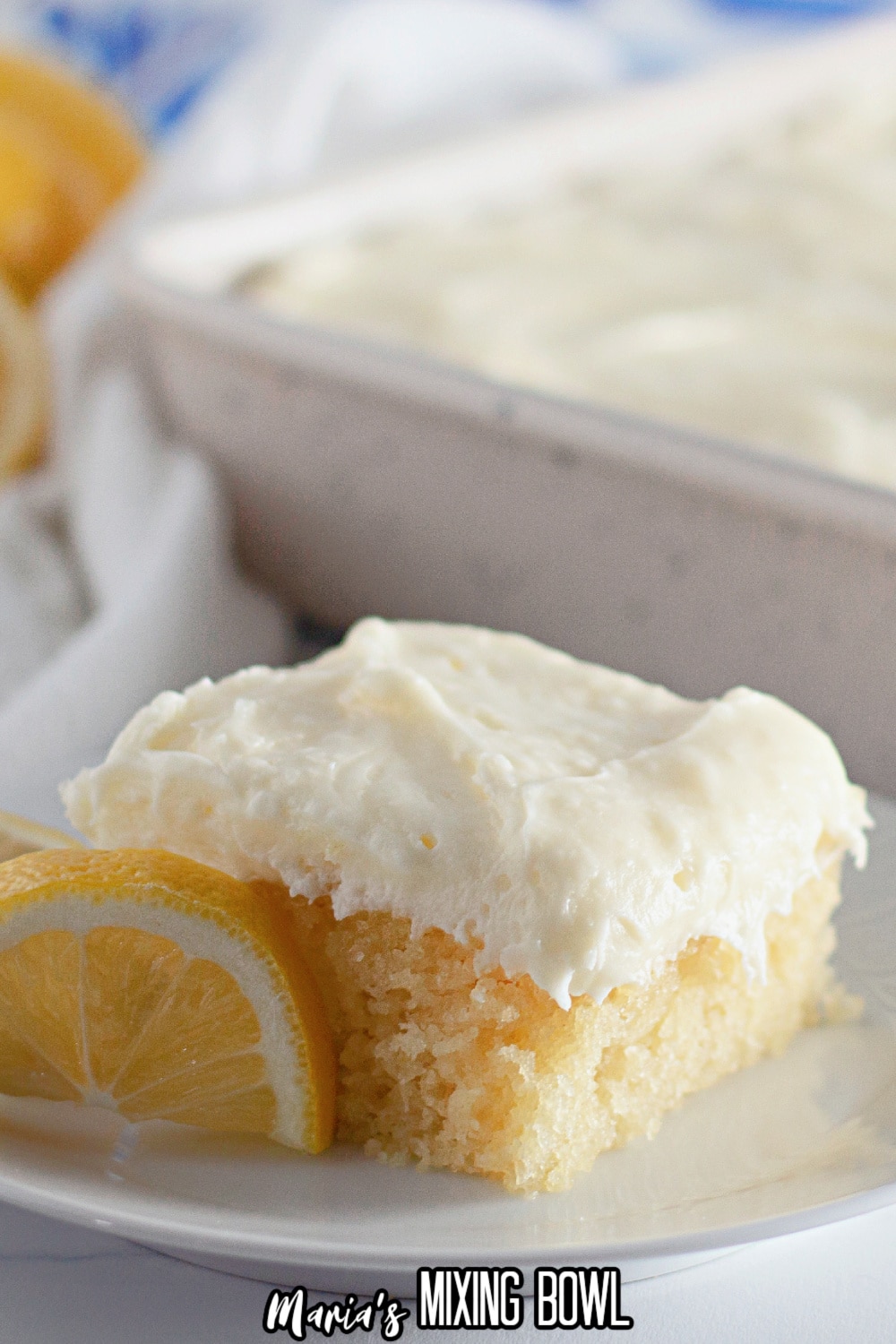 slice of lemon crazy cake frosting with cream cheese frosting on a white plate with lemon wedges