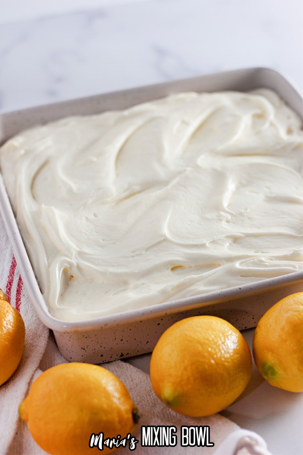 frosted cake in a white cake pan surround by lemons