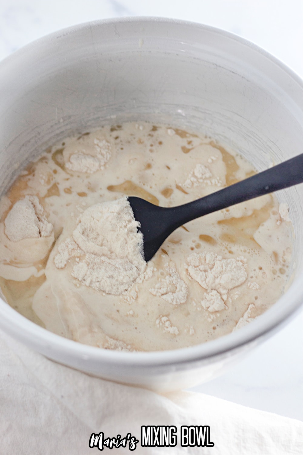 cake batter being mixed with a black rubber spoon in a white mixing bowl